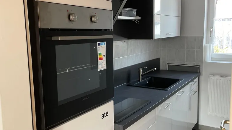 Moderne Küche mit integriertem Backofen, Dunstabzugshaube und Spülbecken, ausgestattet mit hellen und dunklen Schränken.