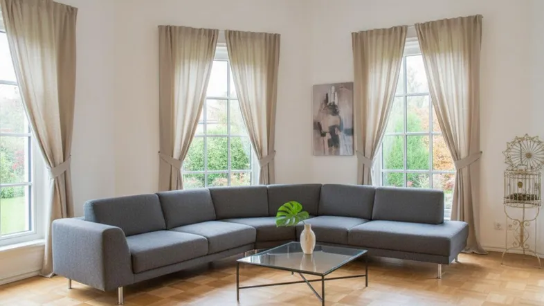 Helles Wohnzimmer mit modernem Ecksofa, Parkettboden und großen Fenstern mit Blick ins Grüne.