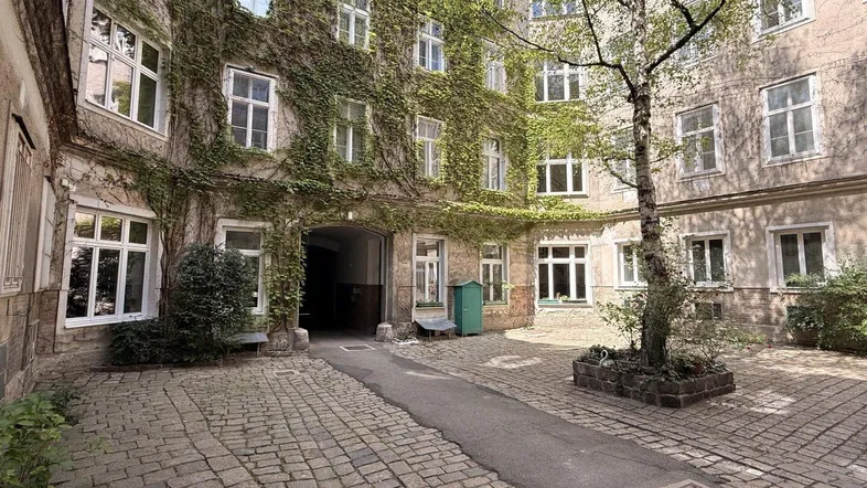 Historischer Innenhof mit Kopfsteinpflaster, bewachsenen Fassaden und einem Baum.