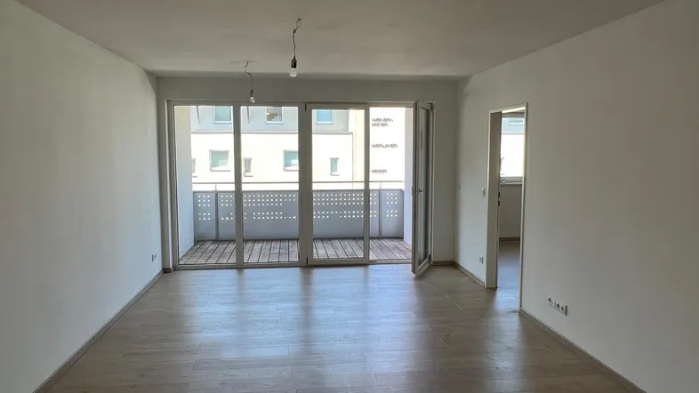 Helles, leeres Wohnzimmer mit Holzboden und Zugang zu einem Balkon, bereit zum Einrichten.