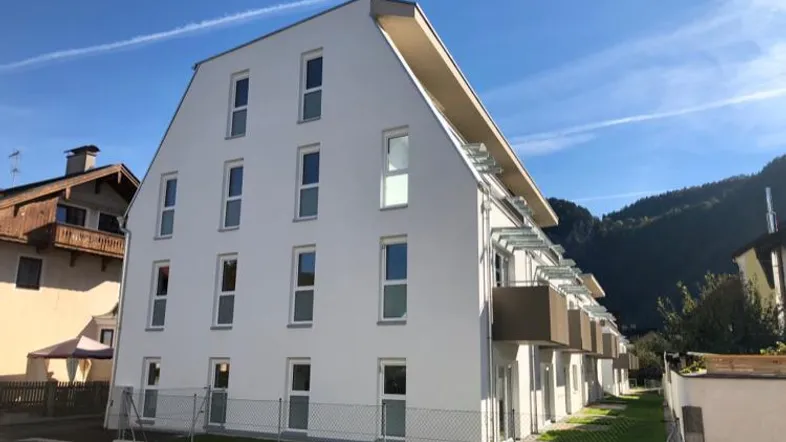 Modernes Mehrfamilienhaus mit weißer Fassade und Satteldach in bergiger Umgebung.