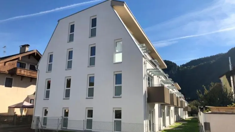 Modernes Mehrfamilienhaus mit weißer Fassade und Balkonen in bergiger Umgebung.
