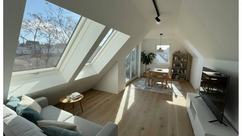 Helles, modernes Wohn-Esszimmer im Dachgeschoss mit Holzboden, Dachfenstern und Blick ins Grüne.