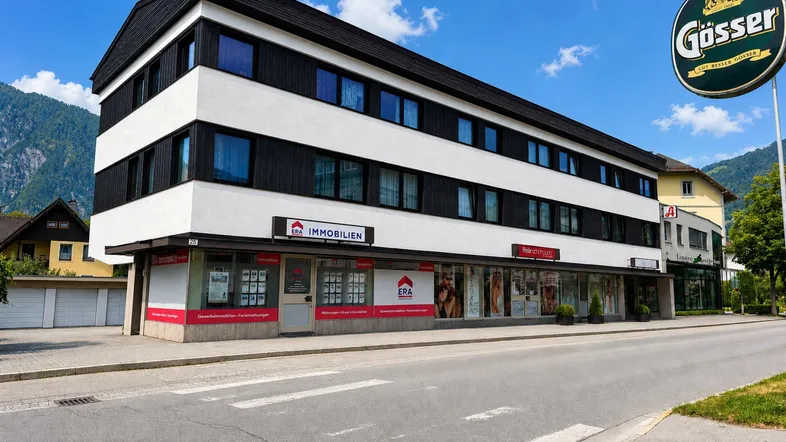 Modernes Geschäftsgebäude mit weißen und schwarzen Fassadenelementen an einer Straße mit Bergkulisse.