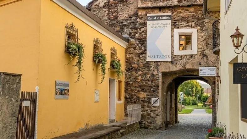 Historische Gasse mit Kopfsteinpflaster, alten Steinmauern und einem gelben Gebäude, das durch einen Torbogen führt.