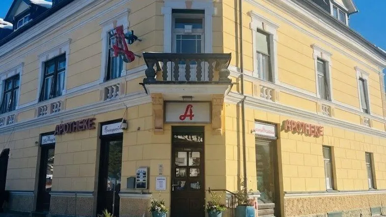 Historisches Eckgebäude mit gelber Fassade und Apotheke im Erdgeschoss, unter blauem Himmel.