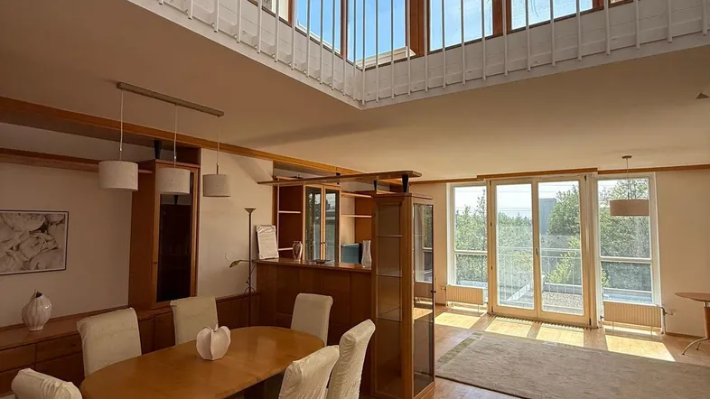Helles Wohn- und Esszimmer mit hohen Decken, Holzfußboden und Zugang zu einem Balkon.