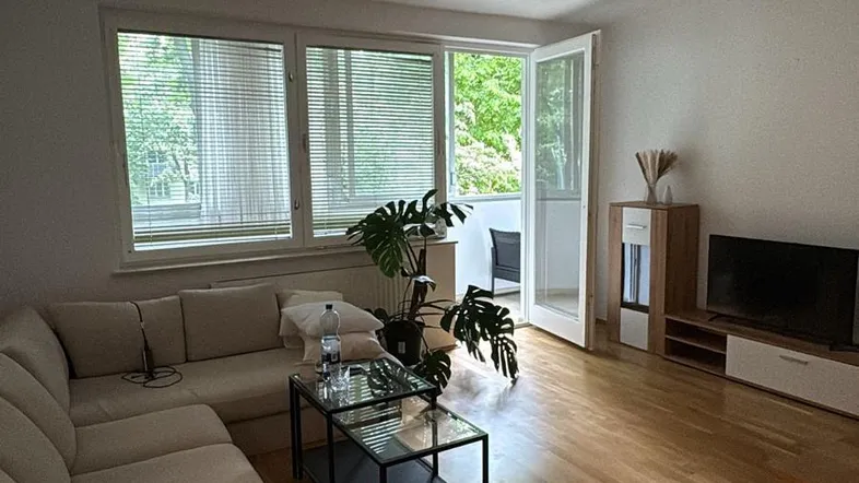 Helles Wohnzimmer mit großem Ecksofa, Holzboden und direktem Zugang zum Balkon.