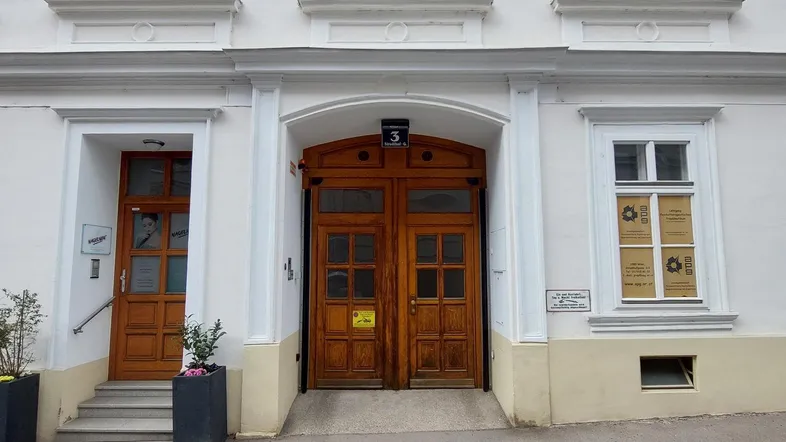 Historische Fassade eines Gebäudes mit eleganten Fenstern und zwei Holztüren im Eingangsbereich.