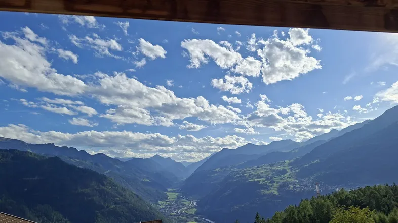 Atemberaubender Blick auf ein grünes Tal und majestätische Berge unter einem blauen Himmel.