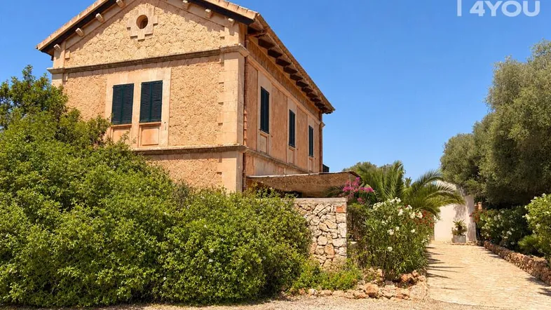 Traditionelles Steinhaus mit grünen Fensterläden und mediterraner Bepflanzung unter blauem Himmel.