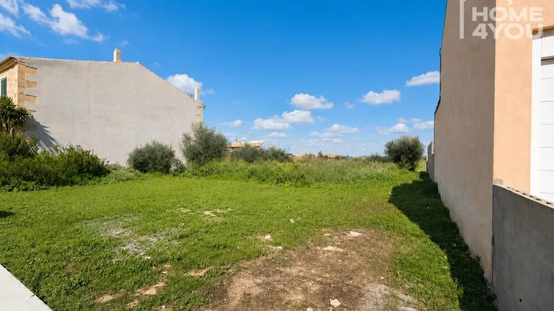 Unbebautes Grundstück mit Grasfläche und umliegenden Gebäuden unter blauem Himmel.