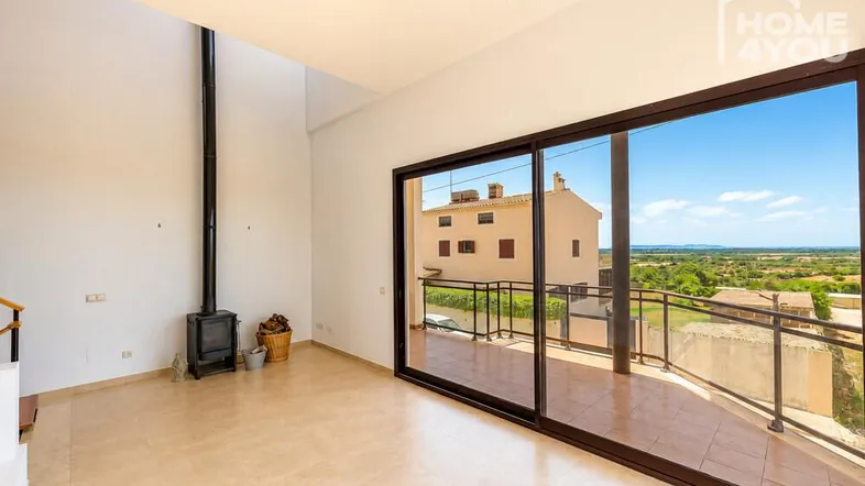 Helles Wohnzimmer mit Kaminofen, hohen Decken und großen Schiebetüren zur Terrasse mit weitem Ausblick.