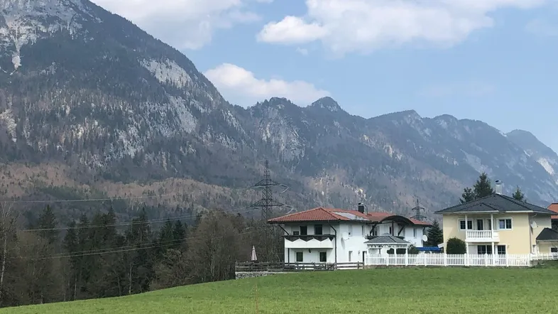 Zwei Wohnhäuser in einer grünen Landschaft mit beeindruckendem Bergblick unter blauem Himmel.
