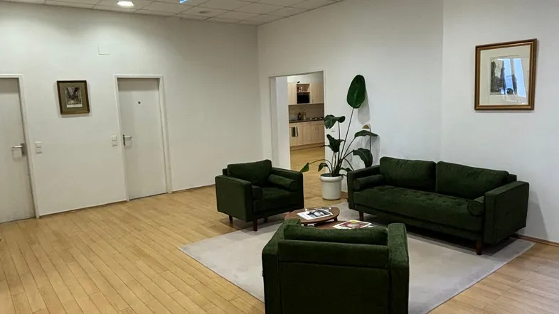 Geräumiger Empfangsbereich mit bequemen grünen Sofas, hellem Holzfußboden und Rasterdeckenbeleuchtung.