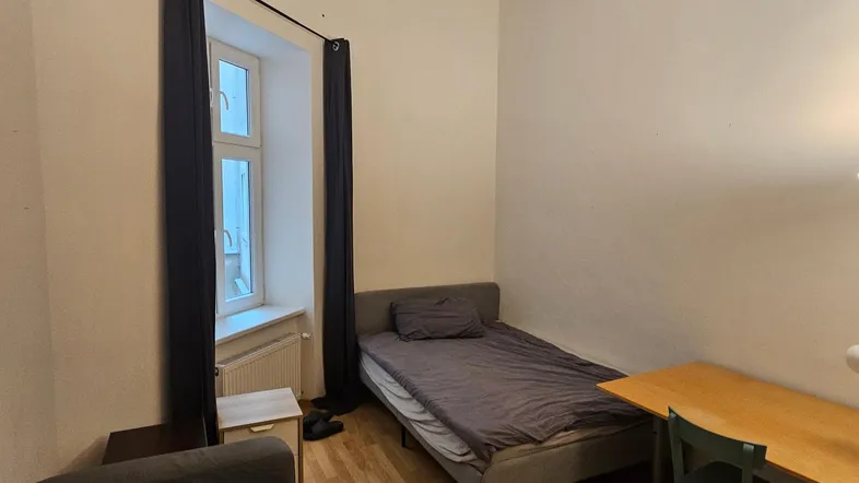 Helles Schlafzimmer mit Einzelbett, Schreibtisch und Holzboden, ideal für Studenten oder Einzelpersonen.