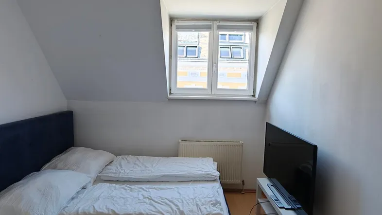 Gemütliches Schlafzimmer im Dachgeschoss mit schräger Decke, Doppelbett und Fernseher.