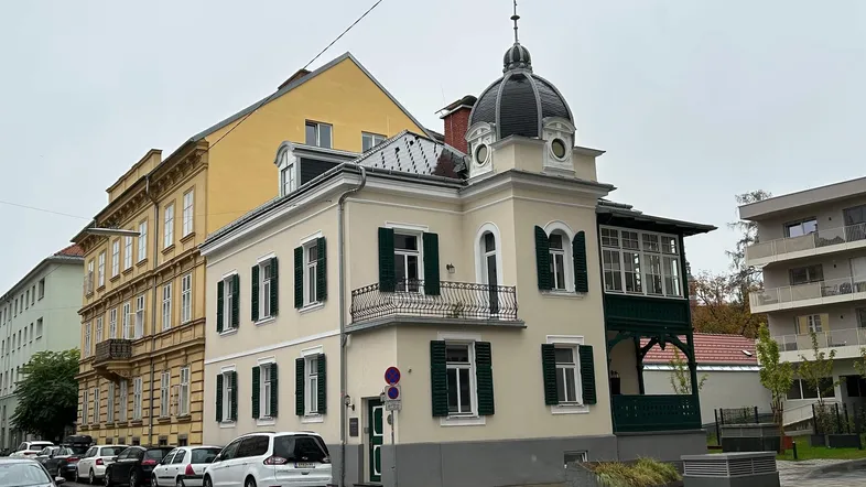 Historisches Gebäude mit markanter Kuppel und grünen Fensterläden an einer belebten Straße.