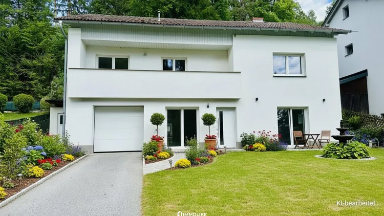 Weißes Einfamilienhaus mit Garage, gepflegtem Vorgarten und blühenden Blumenbeeten.