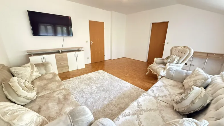 Geräumiges Wohnzimmer mit beigem Sofa, Parkettboden und Dachschräge, ideal zum Entspannen.
