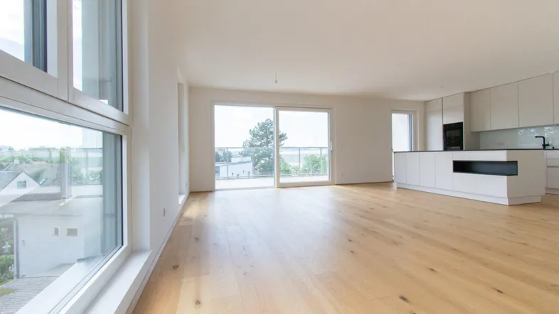 Heller offener Wohnbereich mit moderner Einbauküche, Holzboden und Zugang zum Balkon.