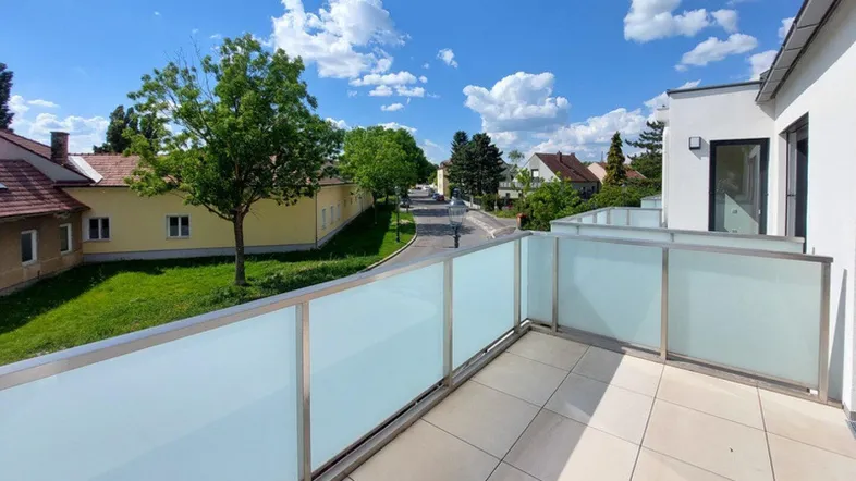 Heller Balkon mit moderner Glasbrüstung und Blick auf die grüne Umgebung.