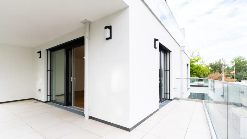 Moderne Terrasse mit Glasgeländer und Zugang zu den Innenräumen, ideal für entspannte Stunden im Freien.