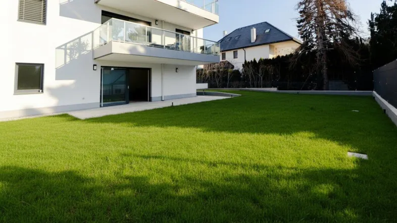 Moderner Neubau mit weißer Fassade, Balkonen, Terrasse und großem, gepflegtem Rasenbereich.