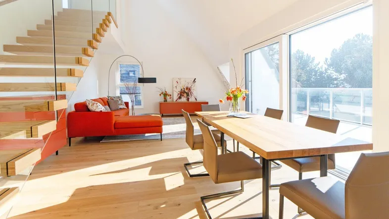Helles, offenes Wohn-Esszimmer mit moderner Holztreppe und großen Fenstern, die viel Tageslicht hereinlassen.