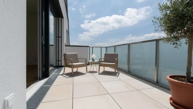 Geräumige Terrasse mit modernen Fliesen, Glasgeländer und bequemen Sitzgelegenheiten unter blauem Himmel.