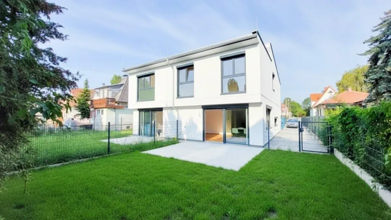 Modernes Einfamilienhaus mit weißer Fassade, großem Garten und sonniger Terrasse.