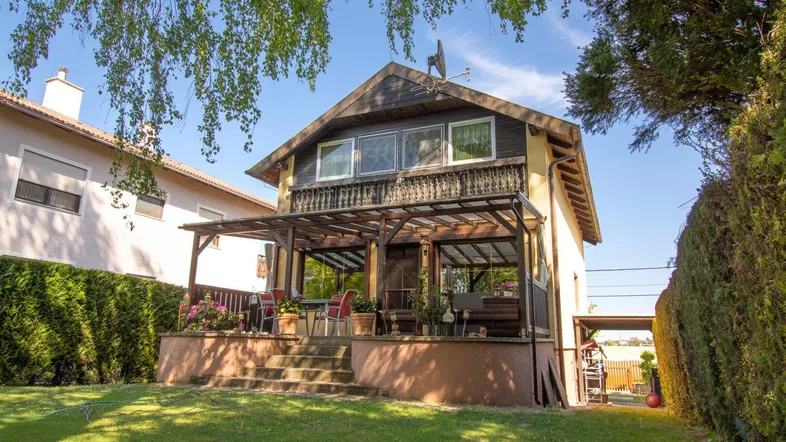 Charmantes Einfamilienhaus mit überdachter Terrasse und gepflegtem Garten unter blauem Himmel.