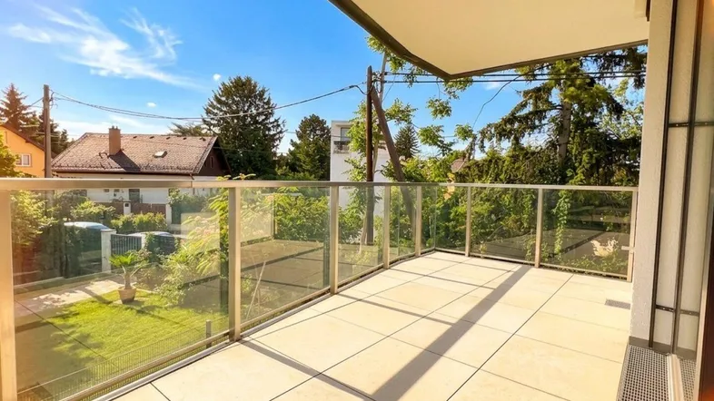 Heller Balkon mit Glasgeländer und Fliesenboden, bietet einen schönen Ausblick ins Grüne.