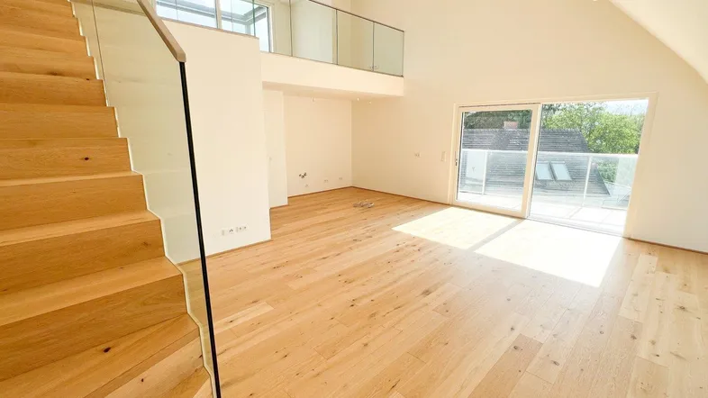 Helles, offenes Wohnzimmer mit Holztreppe, Galerie und Zugang zu einem sonnigen Außenbereich.