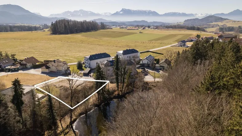 Luftaufnahme eines Grundstücks in ländlicher Umgebung mit Fluss und Bergblick im Hintergrund.