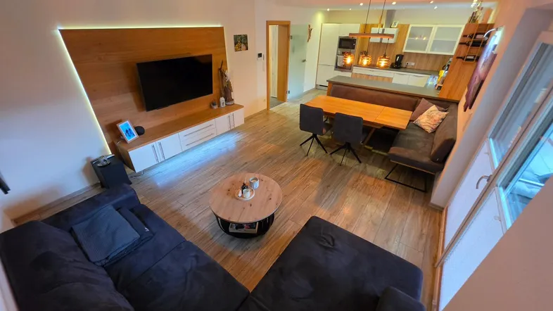 Moderner Wohn-Essbereich mit integrierter Küche, Holzboden und stilvoller TV-Wand.