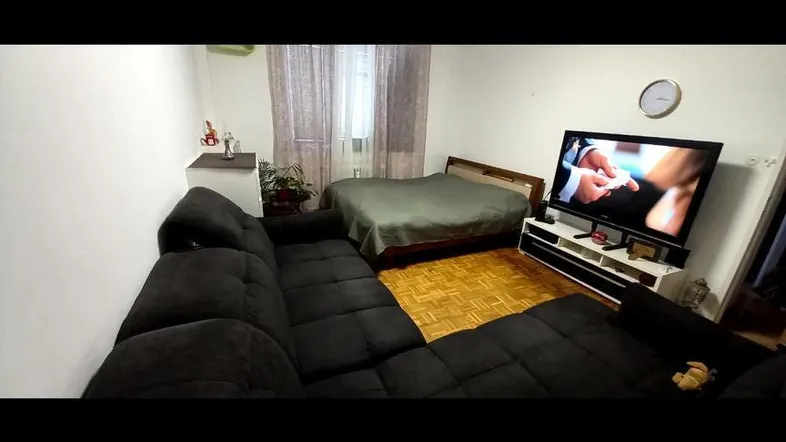 Geräumiges Wohnzimmer mit großem Ecksofa, Fernseher und Schlafbereich im Hintergrund.