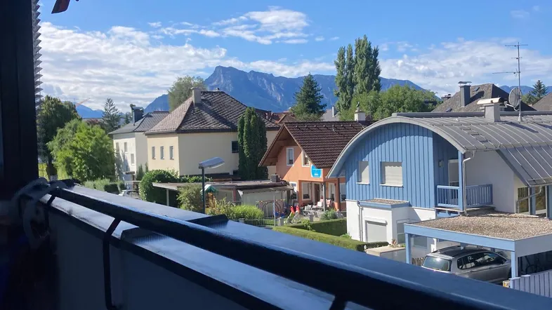 Panoramablick vom Balkon auf die umliegende Wohngegend mit Bergen im Hintergrund und blauem Himmel.