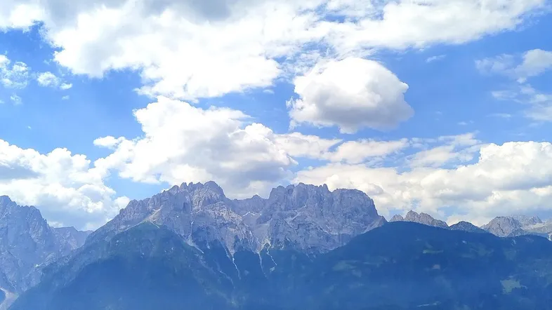 Panoramablick auf majestätische Berge und ein grünes Tal unter einem weiten blauen Himmel.