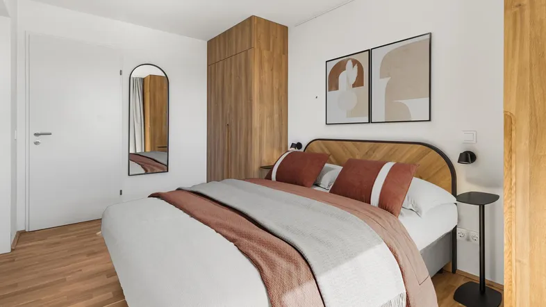 Modernes Schlafzimmer mit Holzboden, großem Bett und integriertem Kleiderschrank, hell und einladend gestaltet.