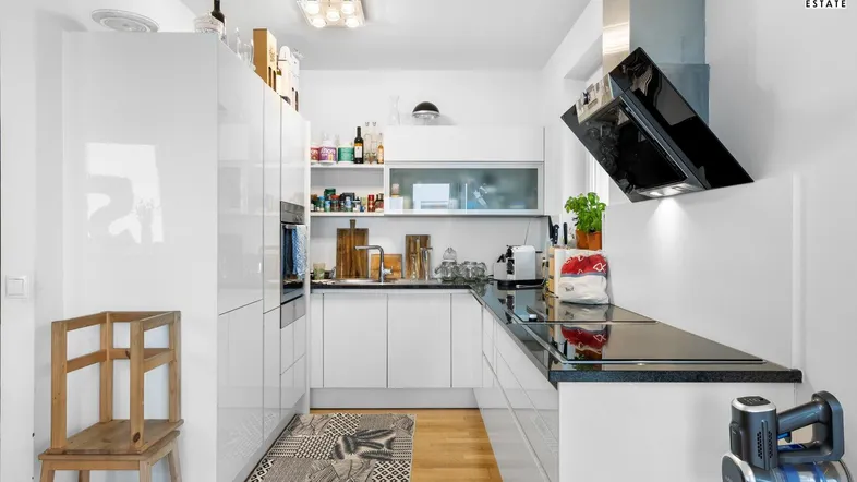 Moderne Küche mit weißen Hochglanzfronten, dunkler Arbeitsplatte und integrierten Geräten.