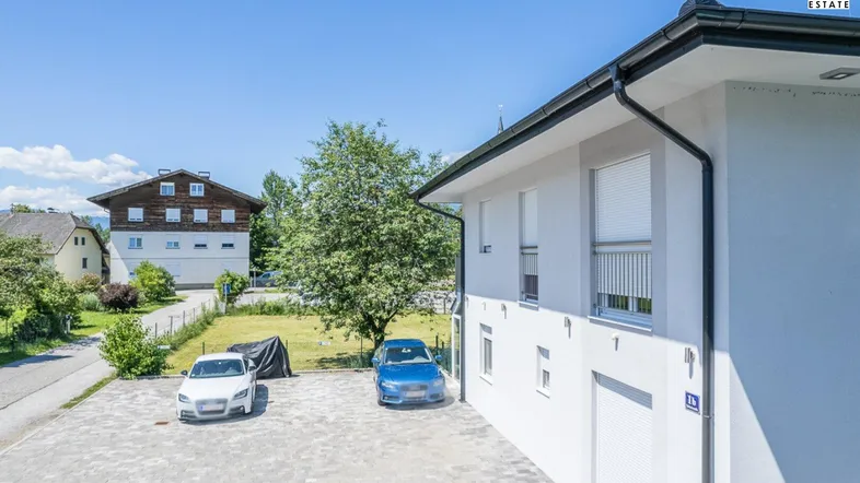 Moderne Hausfassade mit gepflastertem Parkplatz und Blick auf die Umgebung.