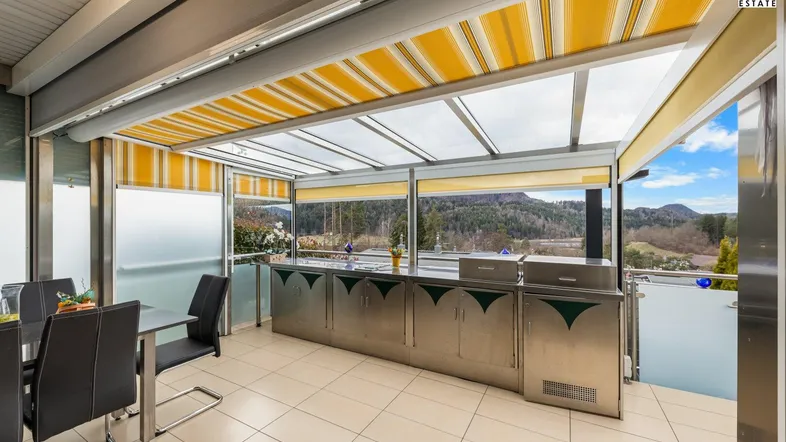 Geräumige verglaste Terrasse mit Essbereich, Außenküche und Panoramablick auf die Landschaft.