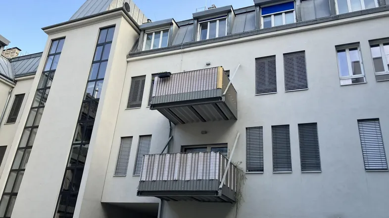 Modernes Gebäude mit mehreren Balkonen und einem externen Glasaufzug an der Fassade.