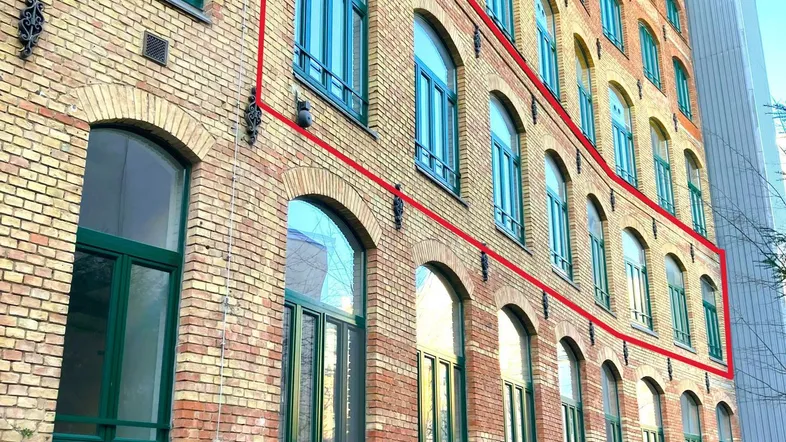 Historisches Backsteingebäude mit vielen Bogenfenstern und einer roten Markierung der oberen Etagen.