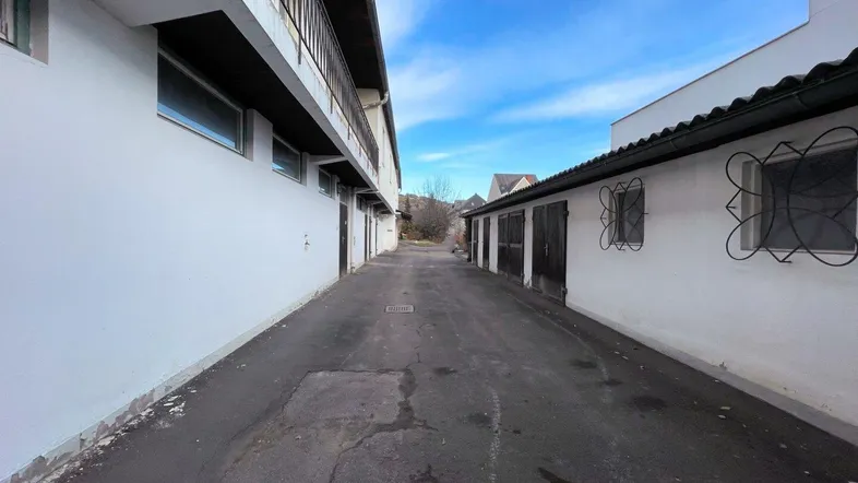 Schmale Gasse zwischen zwei Gebäuden mit weiß getünchten Wänden und Garagentoren unter blauem Himmel.