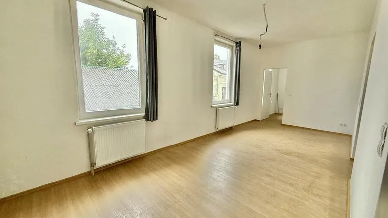 Helles, leeres Zimmer mit Holzfußboden und zwei Fenstern, bereit zur individuellen Gestaltung.