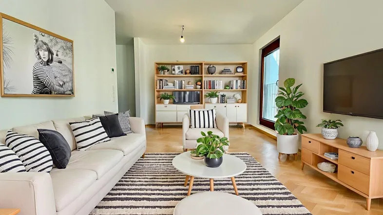 Helles Wohnzimmer mit modernem Mobiliar, Parkettboden und großem Fenster, das viel Tageslicht hereinlässt.