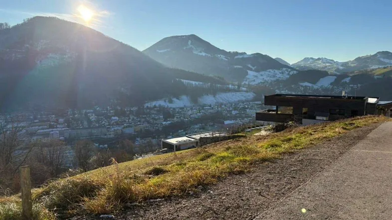 Sonnige Berglandschaft mit modernem Gebäude auf einem Hang und Blick auf die darunterliegende Stadt.