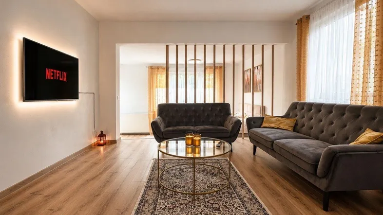Modernes Wohnzimmer mit Holzboden, bequemen Sofas und einem beleuchteten Fernseher.